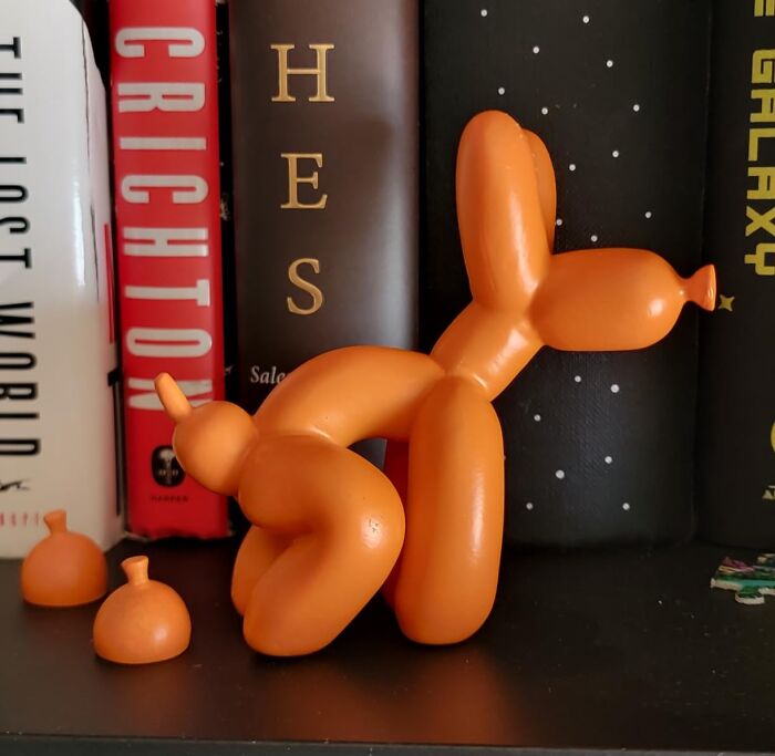 Orange chaotic product shaped like a balloon dog on a shelf next to books, showcasing a unique and quirky design.