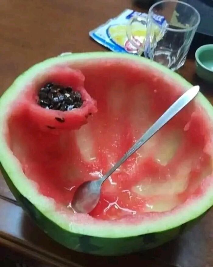 Half-eaten watermelon with spoon and seeds, showcasing creative culinary presentation.