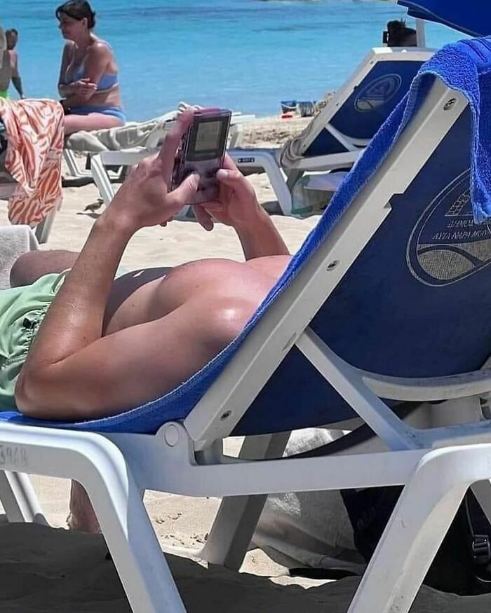 Person playing a Game Boy on a lounge chair at the beach, embodying the "pics that go hard" aesthetic.