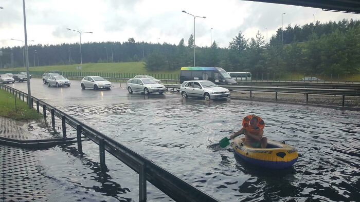 Flooded road with cars stuck and a person paddling a small inflatable boat showing nature's wild impact.