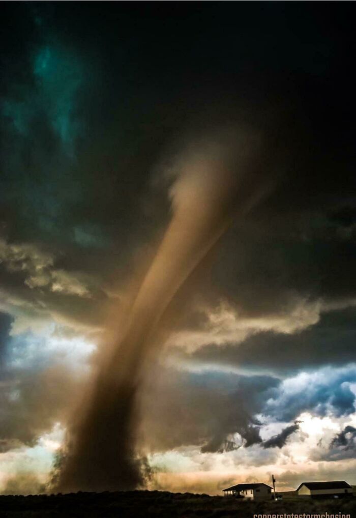 Tornado touching down near houses under dark, stormy skies showcasing wild nature's raw power.