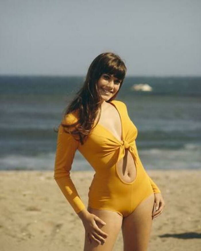 Young woman in a yellow swimsuit posing on the beach, evoking nostalgia and creaking joints memories for older generations