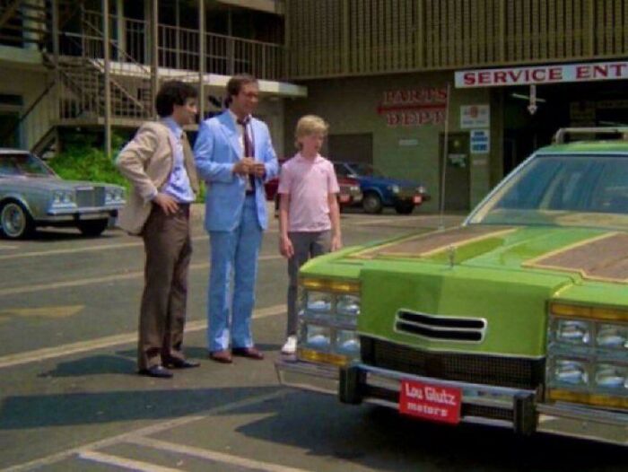 Three men standing beside a vintage green car outside a service center, evoking nostalgia and old memories.