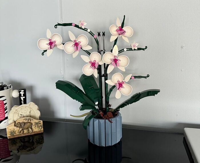Lego orchid plant with white and pink flowers in a blue vase on a black surface, featured in TikTok finds collection.
