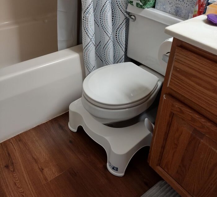 Bathroom with white toilet on a stool, wooden floor, and a shower curtain featuring a geometric pattern.