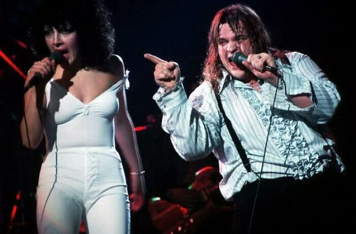 Performers singing on stage wearing vintage 1980s style clothing, evoking nostalgia and creaking joints memories.