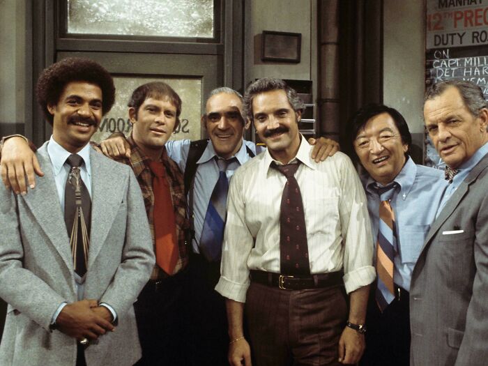 Group of six men in vintage office attire smiling together, evoking nostalgia and creaking joints memories.