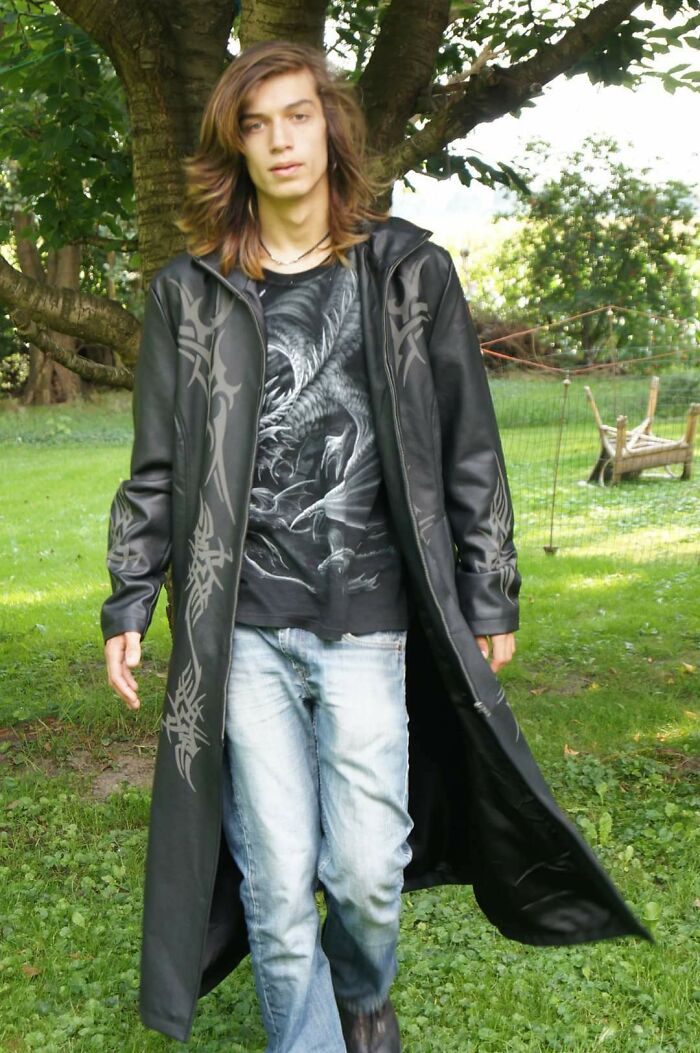 Teen boy wearing a long black coat and graphic t-shirt outdoors, a cringy childhood photo with alternative fashion style.