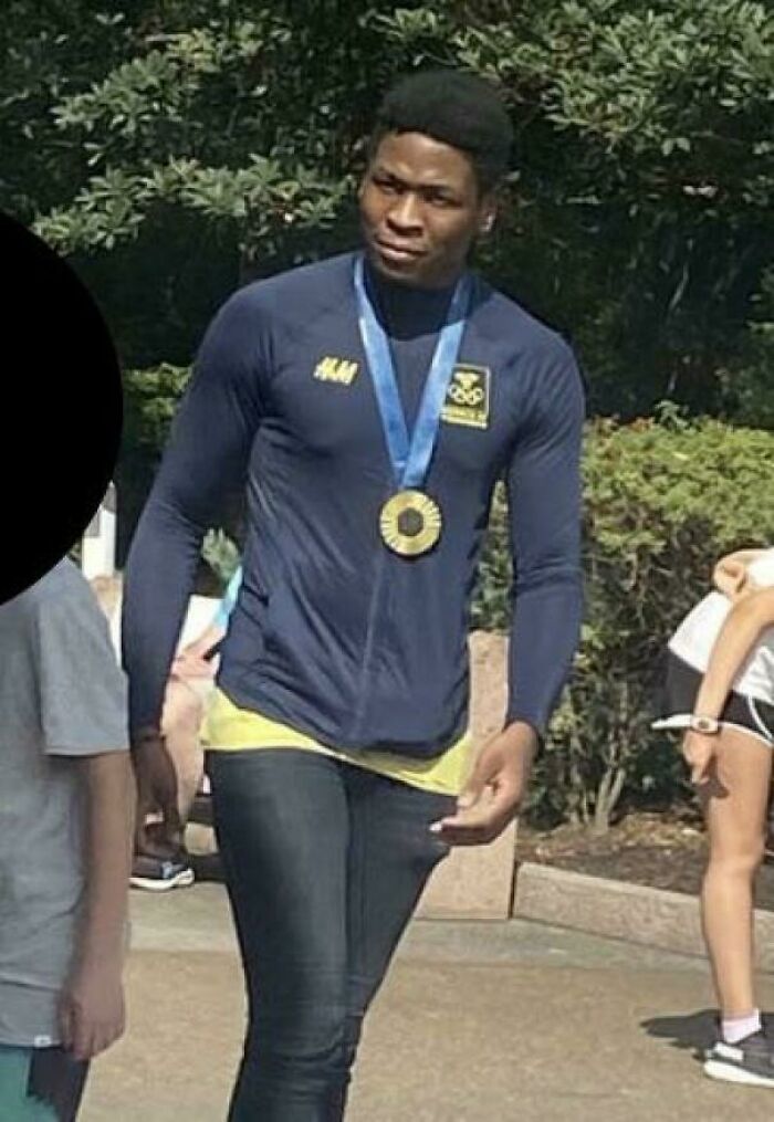 Person wearing a medal and sportswear, confidently walking outdoors, appearing to belong in a competition setting.