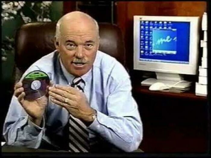 Older man holding a CD-ROM in an office setting, a nostalgic item that may remind you of creaking joints and past technology.