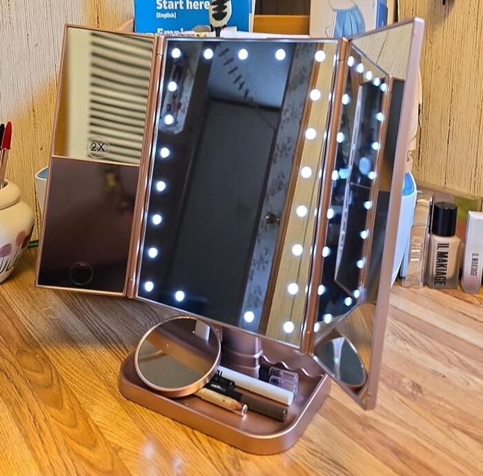 LED lighted tri-fold makeup mirror on a wooden desk with small beauty products, ideal for dorm room organization.