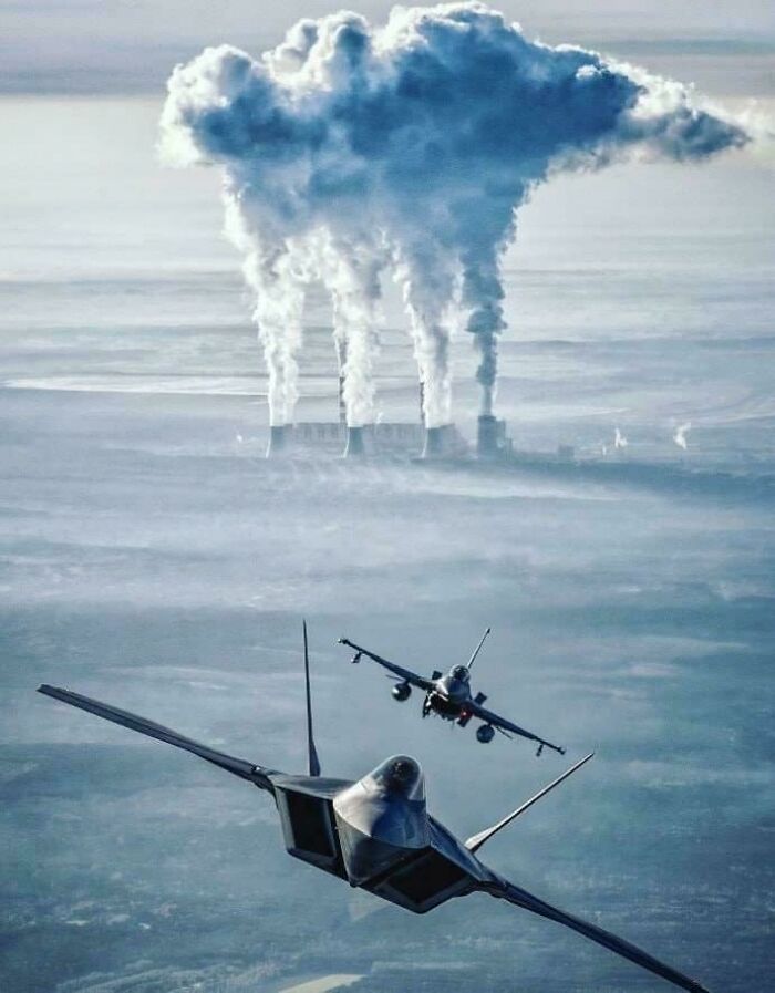 Two fighter jets flying over a foggy landscape with large industrial smoke stacks creating a giant cloud, striking fear for megalophobia.