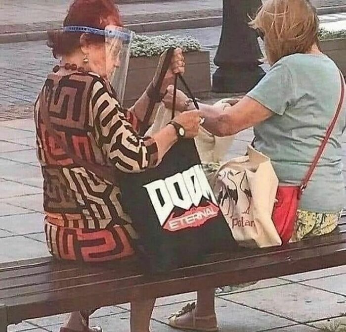 Two women on a bench, one holding a "Doom Eternal" tote, showcasing "Pics That Go Hard" humor.