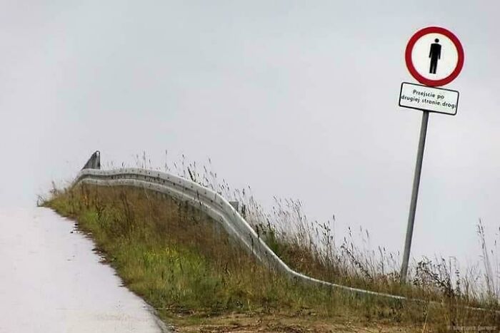 Confusing pic of a warped guardrail with a pedestrian sign on a foggy road.