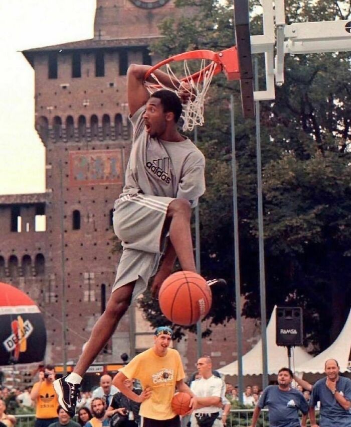 '90s basketball player performing a slam dunk at an outdoor event, surrounded by spectators.