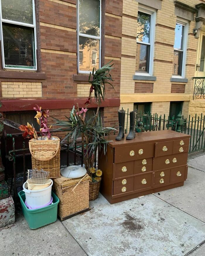 Curbside treasure in NYC: dresser, baskets, and boots left on sidewalk against a brick building for others to find.