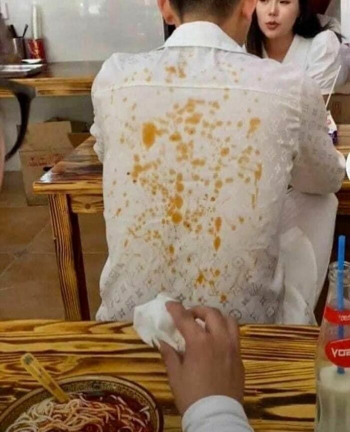 Man with a heavily stained white shirt sitting at a table in a restaurant, showing random photos for processing challenges.