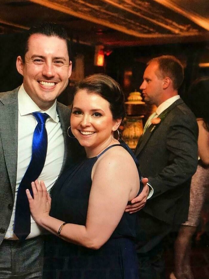 Couple smiling at event while a third person appears to hold a cake oddly, a seriously confusing perspective.