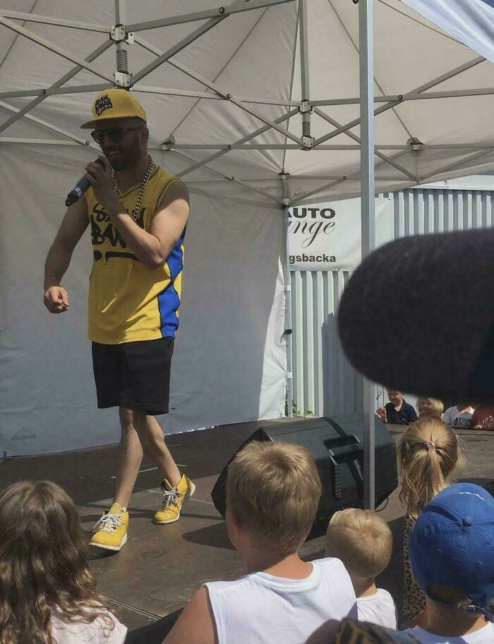 Man in yellow and blue outfit performing on stage, while a microphone shadow creates a confusing perspective effect.
