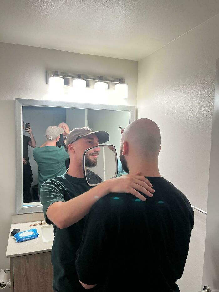 Man holding a mirror in a bathroom creating a confusing visual illusion with a reflection.