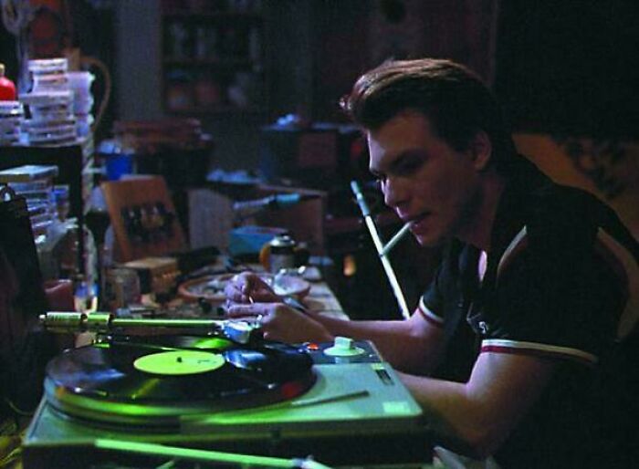 Young man listening to vinyl records in a dimly lit room, evoking nostalgia and creaking joints memories.