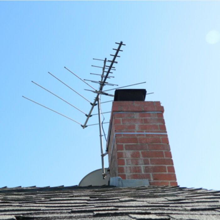 Old rooftop TV antenna mounted on a brick chimney under clear blue sky, reminding of creaking joints nostalgia.