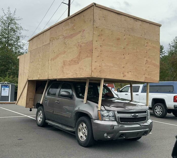 Chevy SUV with large unstable DIY wooden structure attached, showcasing a major DIY disaster on a street parking lot.