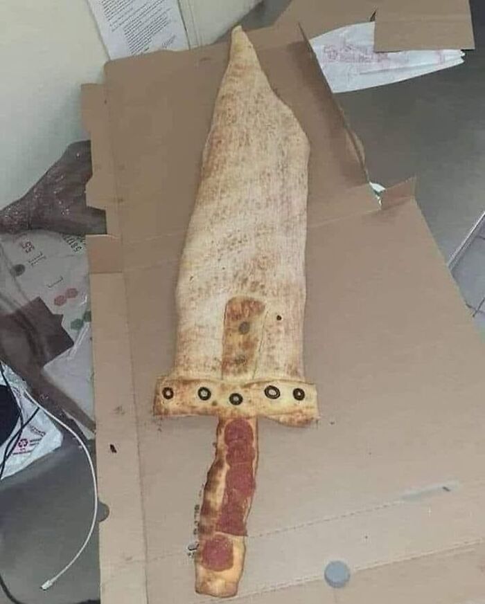 Sword-shaped pizza with pepperoni handle in a cardboard box, representing creative food art from the "Pics That Go Hard" trend.