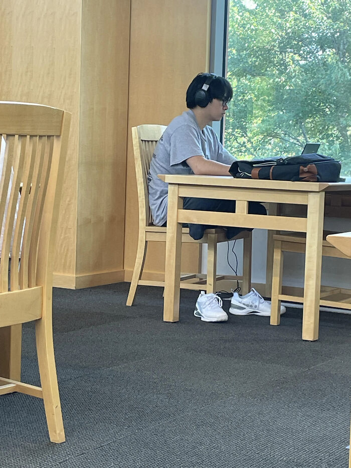 Person at table with headphones, appears to have removed shoes, creating confusing perspective.