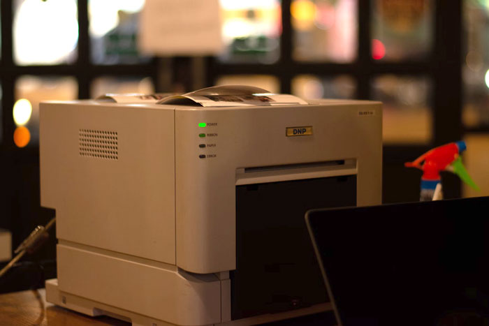 Close-up of a DNP printer with indicator lights on in a dimly lit room, highlighting embarrassing attempts at understanding computers.