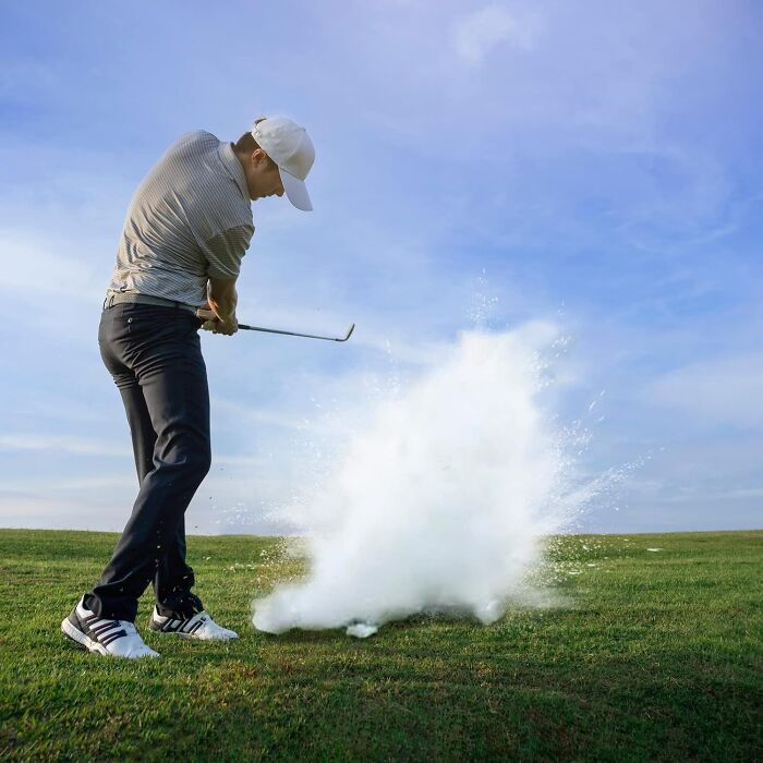 Golfer hits ball, creating cloud of white powder, as part of a playful prank on the golf course.
