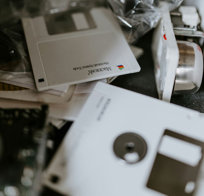 Close-up of vintage Macintosh floppy disks scattered on a desk, highlighting early computer technology and tools.