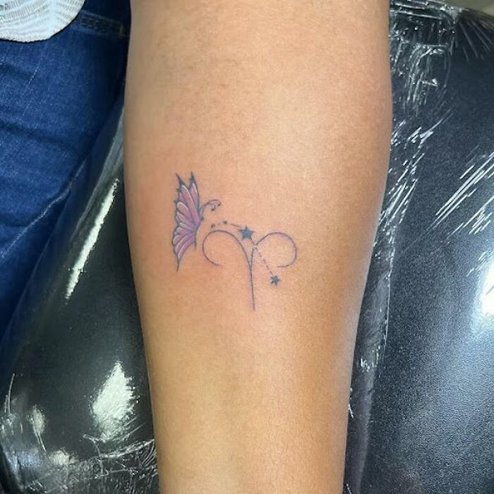 Bold Aries tattoo with stars and butterfly on an arm, aligned with cosmic design elements.