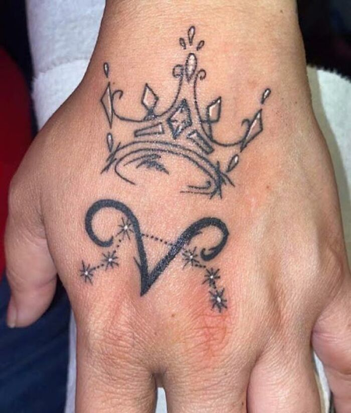 Aries tattoo with a crown design on a hand, featuring starry constellation accents.