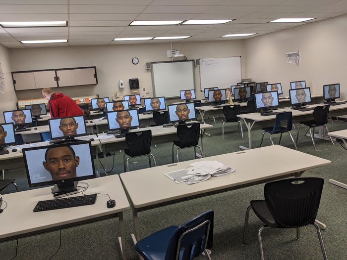 Computer lab monitors displaying Tyler The Creator mugshot, person in red hoodie adjusting a computer.