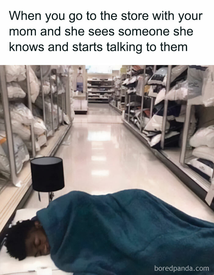 Waiting meme: Person lying on store aisle floor with a blanket and lamp, humorously illustrating boredom while waiting.