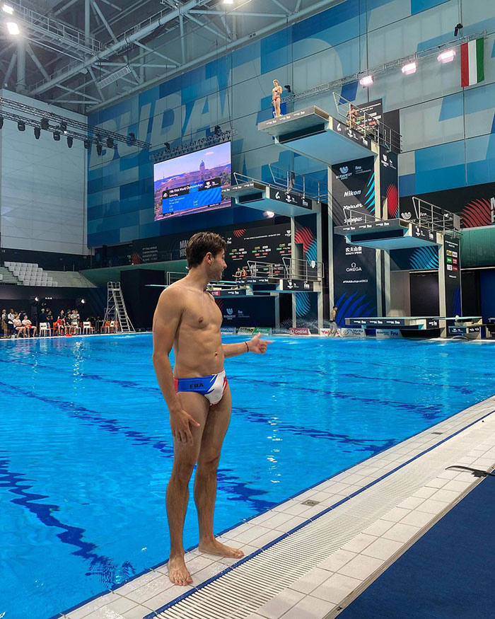 Olympic diver beside pool, with diving platforms in background, in a swim brief during a competition event. Olympic diver beside pool, with diving platforms in background, in a swim brief during a competition event.