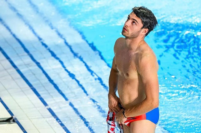 Olympic diver adjusting swimwear by poolside, looking up, in a colorful swimsuit. Olympic diver adjusting swimwear by poolside, looking up, in a colorful swimsuit.