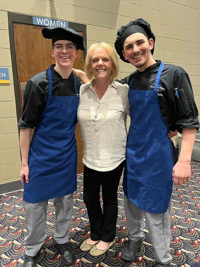 Teacher with two smiling students in chef attire, capturing a heartfelt moment.