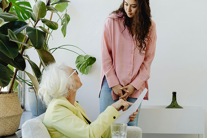 Older woman talking to younger woman holding a paper, illustrating an example of helicopter parenting behavior.