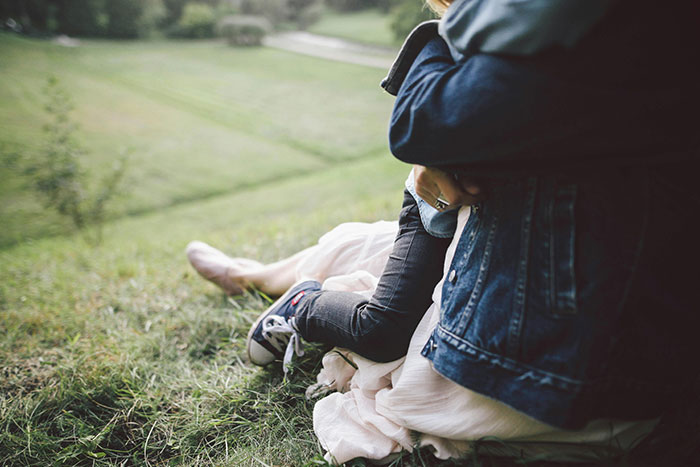 Parent tightly holding child on grassy hill, illustrating examples of helicopter parenting in an outdoor setting.