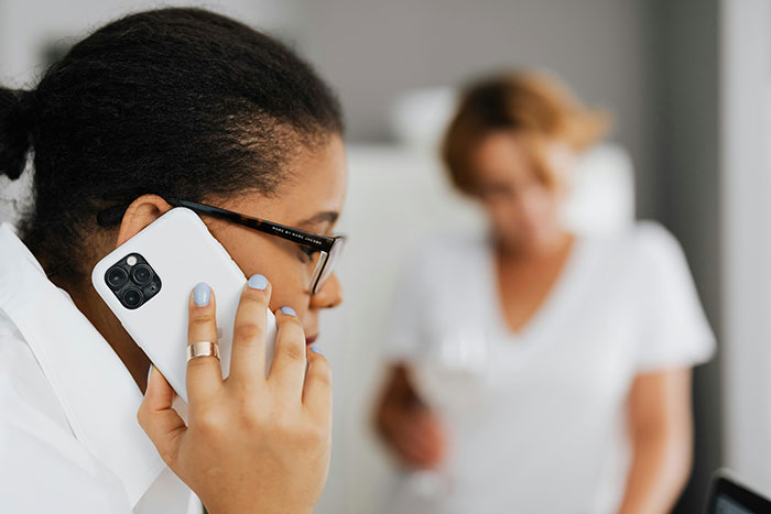 Woman using a smartphone indoors with blurred adult in background, illustrating the concept of helicopter parenting examples.