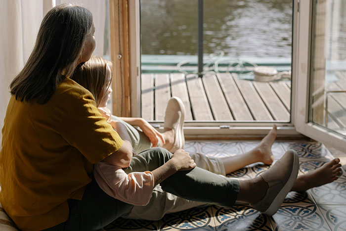 Mother and child sitting by the window overlooking water, illustrating a moment related to helicopter parenting behavior.