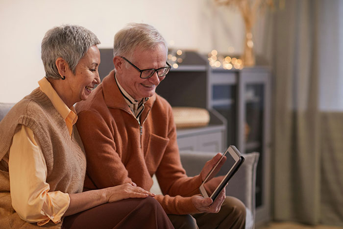 Elderly couple smiling together while looking at a tablet, illustrating a moment related to helicopter parenting examples.