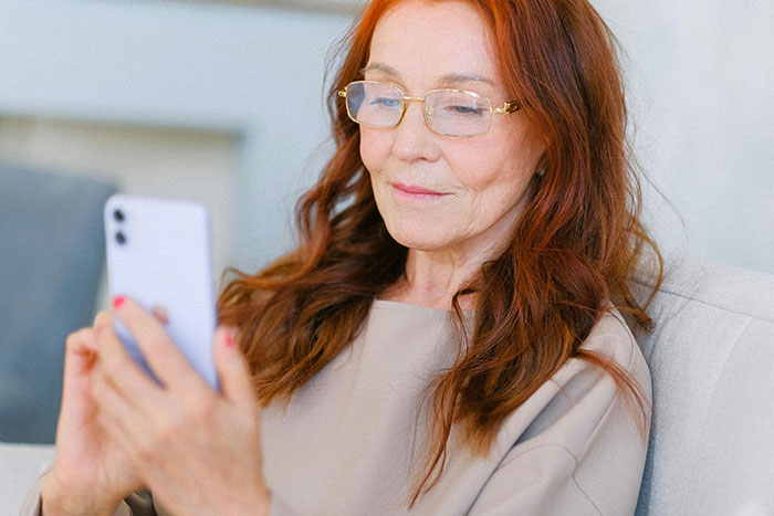 Woman with glasses using smartphone on couch, illustrating a moment related to helicopter parenting behavior.