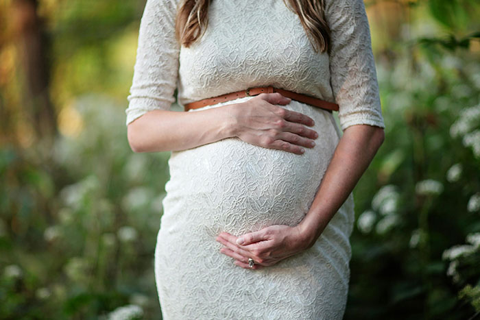 Pregnant woman gently holding belly outdoors, illustrating themes related to helicopter parenting concerns and family care.