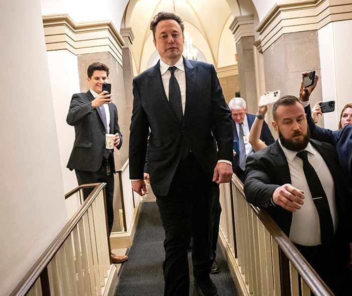 Man in a suit walking through a hallway, accompanied by people taking photos, related to legal battle over children.