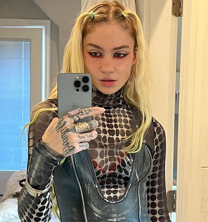 Grimes taking a mirror selfie in a patterned outfit amid legal battle over children with Elon Musk.
