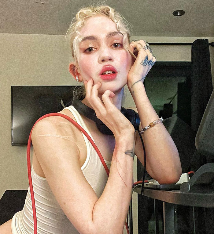 Person with blond hair in a tank top and headphones, related to legal battle over Musk and Grimes&rsquo; kids.