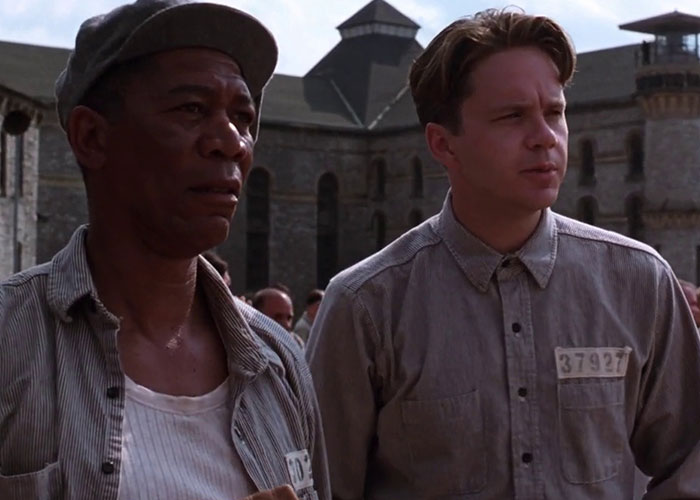 Two men in prison uniforms standing outside a prison, a notable scene from film adaptations that outdid their books.